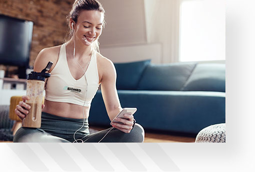 Young female on phone during rest while working out at home, drinking protein shake