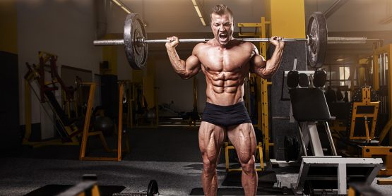 Muscular bodybuilder guy doing exercises with dumbbell in yellow gym