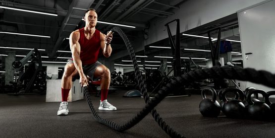 Muscular guy in red tank top doing the ropes at the gym